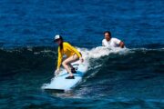 girl catching a wave and surf instructor looking on approvingly.